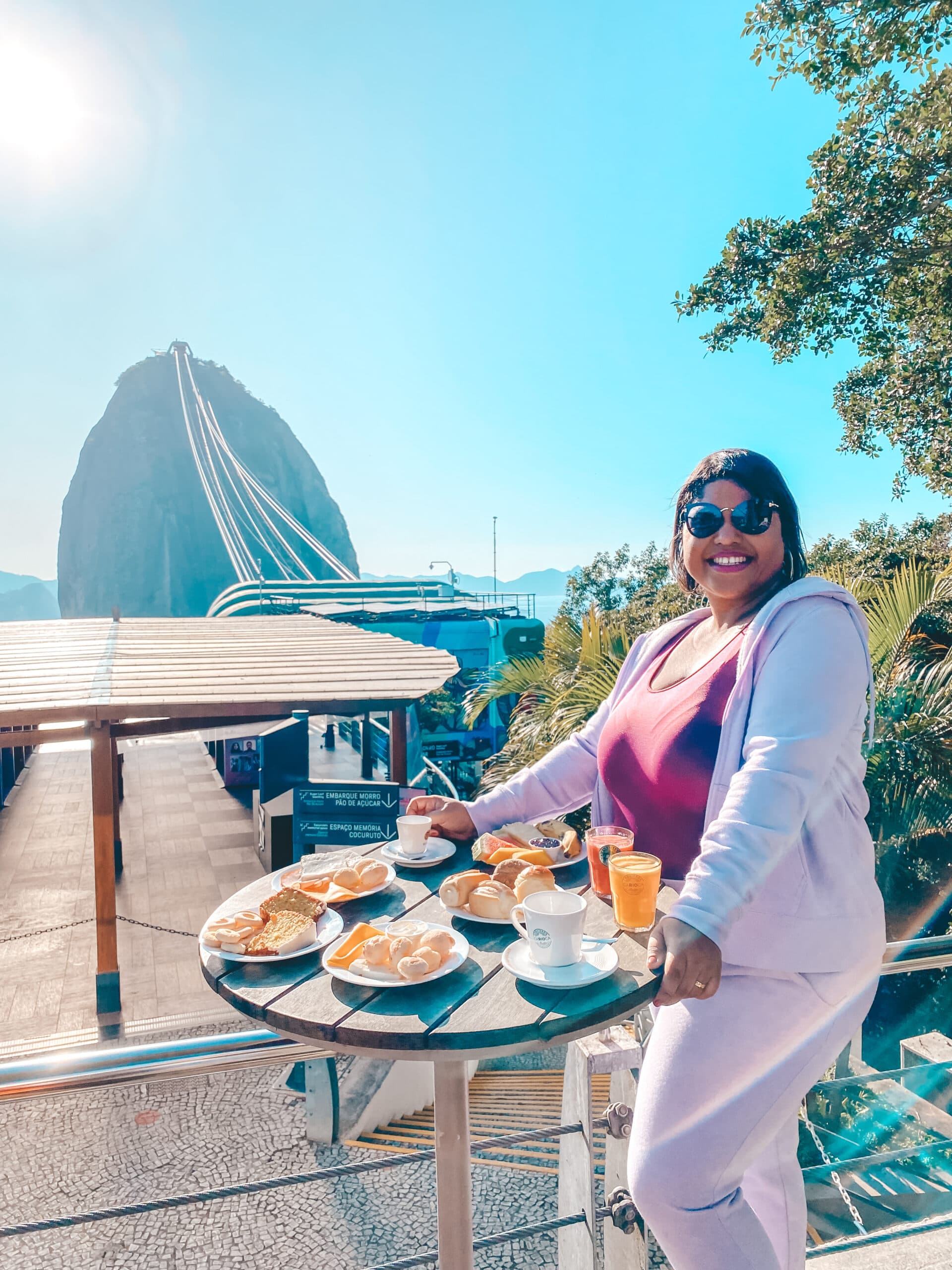 Mulher posando ao lado de uma mesa de café da manhã com o pão de açúcar ao fundo