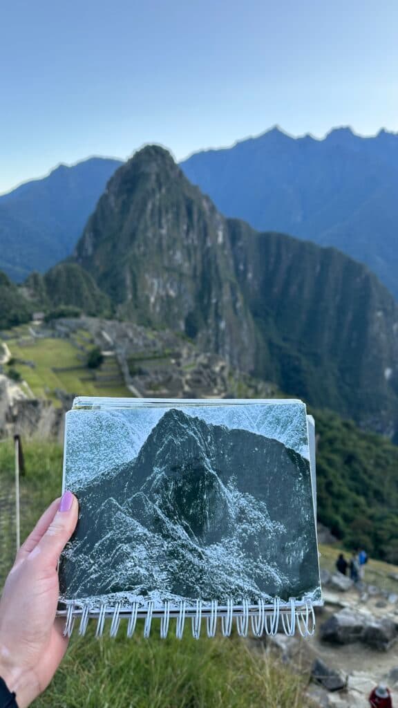 Paisagem ampla e uma mão segurando a foto de uma montanha