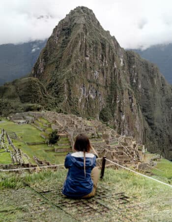 Mulher responsável pelo perfil de Instagram Vai Dormir Onde? sentada no chão. vendo boa parte da cidade perdida, Machu Picchu