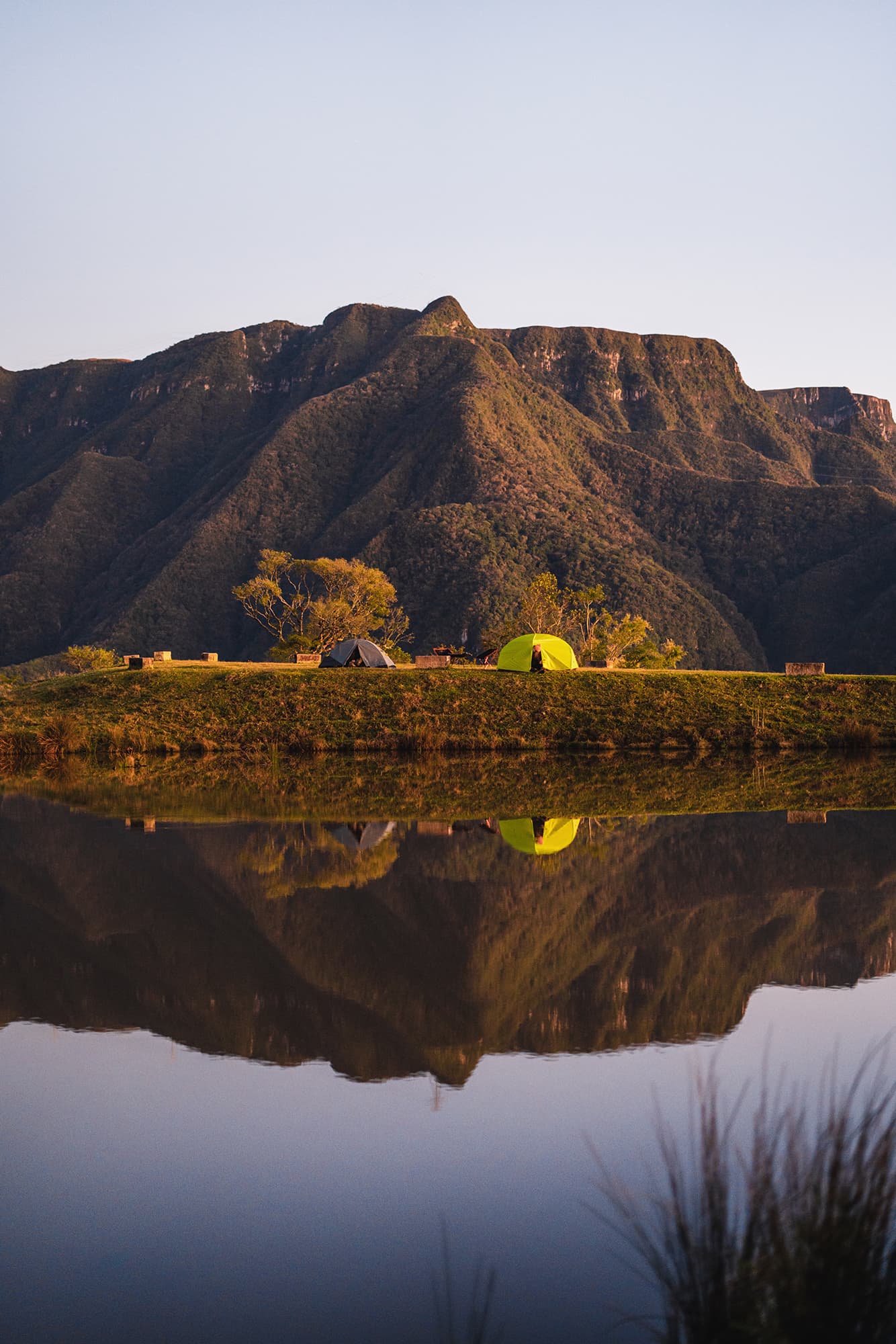 Barracas de camping aos pés da montanha e em frente a um lago