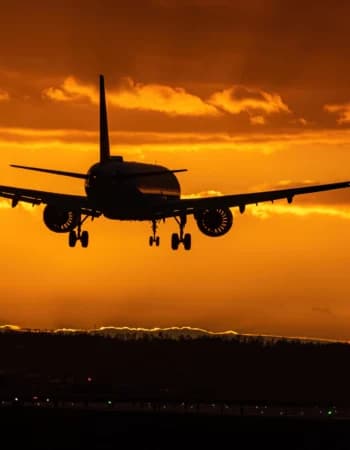 Silhueta de Avião voando com o trem de pouso aberto pronto para pousar depois de um voo na madrugada em um céu dourado num amanhecer com poucas nuvens e raios de sol