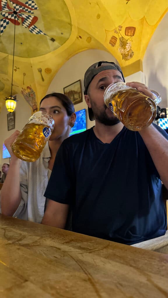 homem de camisa preta e bone com uma mulher morena de camisa branca. Os dois estão bebendo um copão de cerveja em um bar de Las Vegas